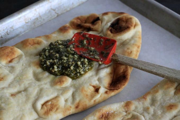 spreading pesto on naan bread for pizza